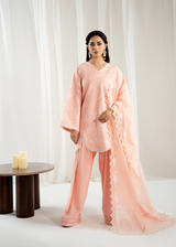 Woman wearing a peach traditional outfit with a sheer dupatta against a white curtain background
